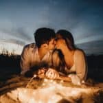 man and woman kissing on brown sand during night time